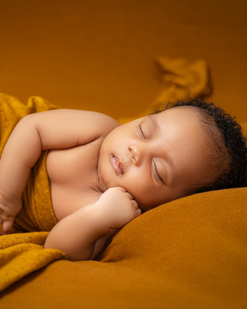Sleeping newborn wrapped in mustard fabric by Javies Photography Studio